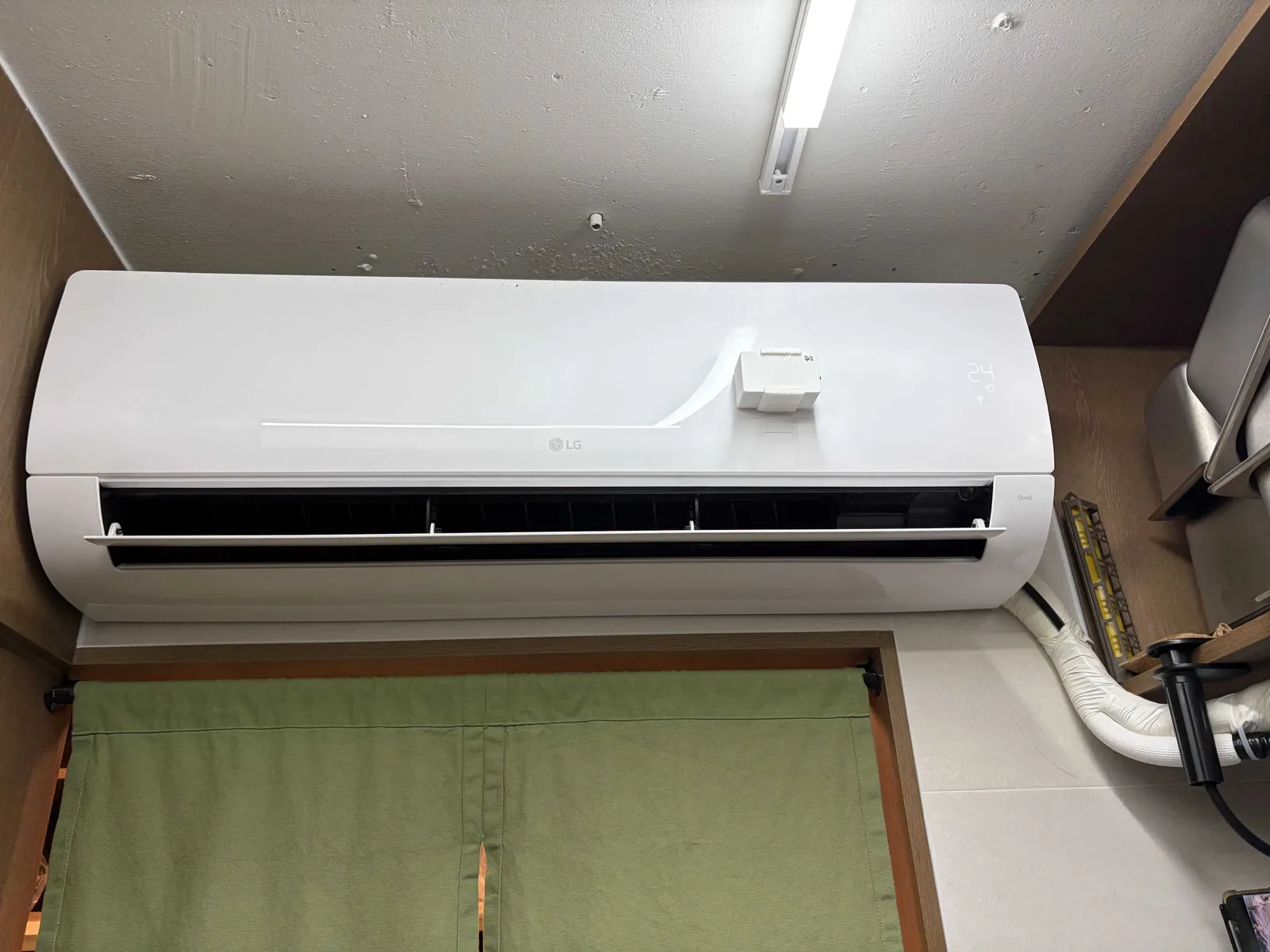 출입구 위 벽에 설치된 벽걸이 에어컨, 본체 앞면에 작은 흰색 컨트롤러 박스가 부착되어 있음